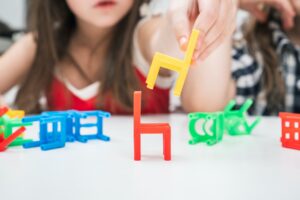 Cropped blurred little girl build pyramid tower from colorful chair toys, play chair ladder tower